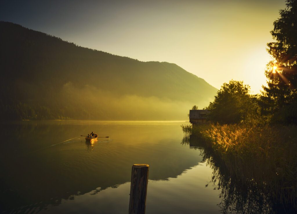 Een boot op een meer tijdens zonsopgang, omringt door bergen en bos