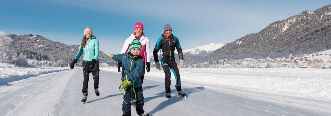 een gezin wat aan het schaatsen is op een bevroren meer met bergen op de achtergrond