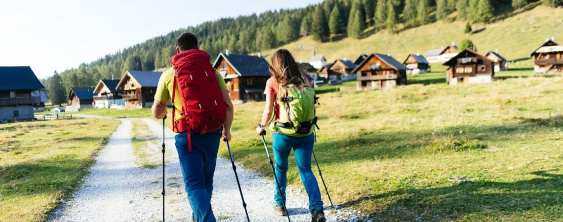 twee mensen die een wandeling maken richting chalets die in de bergen staan
