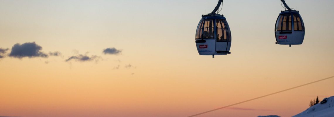 twee gondels van een skilift met op de achtergrond een uitzicht over de bergen tijdens zonsopkomst