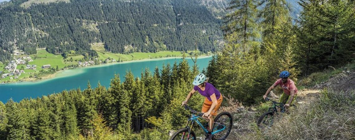 twee mensen die aan het mountainbiken zijn in de bergen met in het dal een meer